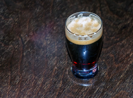 A mug of dark beer foaming on a wooden table.の写真素材