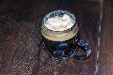 A mug of dark beer foaming on a wooden table.の写真素材