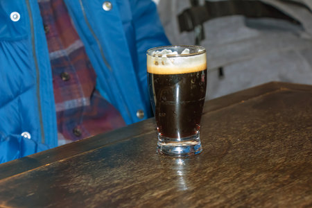 A mug of dark beer foaming on a wooden table.の写真素材