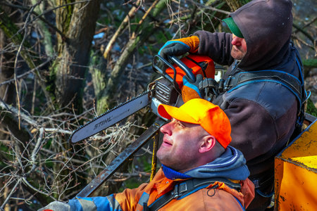 Dnepr, Ukraine - 03.20.2024: Municipal service workers stand with a chainsaw in a crane basket and trim dangerous trees.のeditorial素材