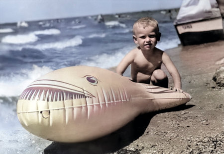 Vintage portrait of a little boy on the seashore. Boy near a big inflatable fish. Retro photo from 1968.の写真素材