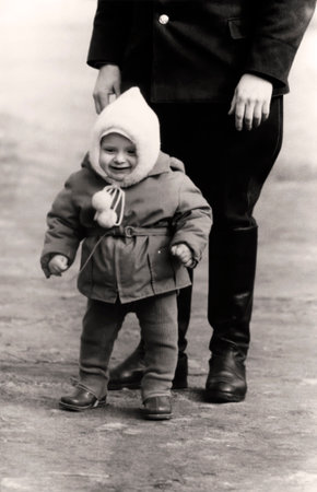 Vintage portrait of a cute little boy in a white cap who is learning to walk with his military dad. Retro photo from 1967.の写真素材