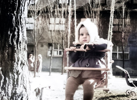 Vintage portrait of cute little boy in white cap riding on swing. Retro photo from 1967.の写真素材