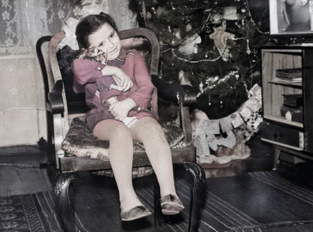Vintage portrait of a little girl with bows sitting in a chair and hugging a doll. Retro photo from 1973.の写真素材