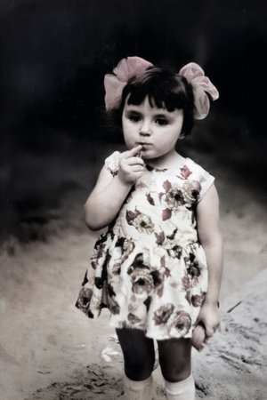 A vintage portrait of a little girl with white bows on her head and a floral dress in summer. Retro photo from 1971.の写真素材