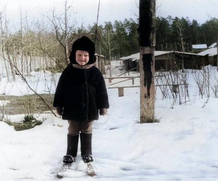 A vintage portrait of a little boy in a fur coat and hat learning to cross-country ski. Retro photo from the 1970s.の写真素材