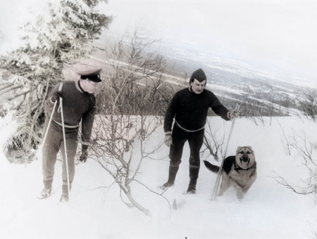Luga, USSR - December 1, 1970: Vintage portrait of two Soviet soldiers on skis and a dog in a snowy forest. Retro photo.のeditorial素材