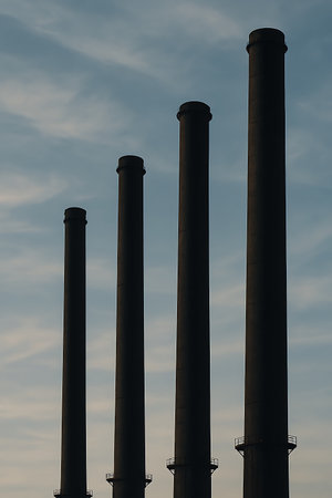 Silhouetted smokestacks rise against a soft, cloudy sky, creating a stark industrial monument scene.の素材