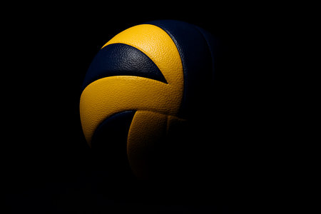 Isolated volleyball with dramatic lighting and textured surface against a stark black backgroundの素材