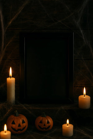 A dark and spooky Halloween scene featuring lit candles, carved pumpkins, and an empty black frame, set against a background of cobwebs and wood.の素材