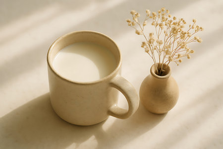 A serene minimalist scene featuring a creamy milk mug and dried flowers in a small vase under soft natural light.の素材
