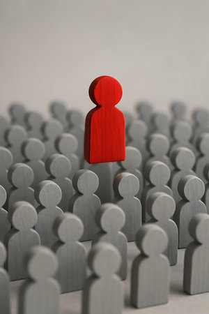 Lone red figure stands tall above a blurred crowd of grey wooden people, representing individuality and leadershipの素材