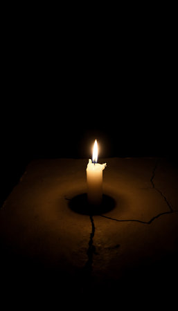 A single candle illuminates a cracked surface in the dark creating a dramatic and hopeful mood.の素材