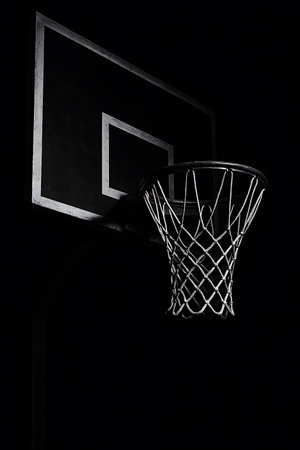 Dramatic monochrome image presents a basketball hoop and backboard against a black backdrop.の素材