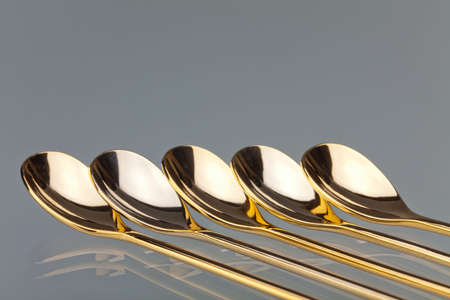Five golden teaspoons lies in a row on the glass