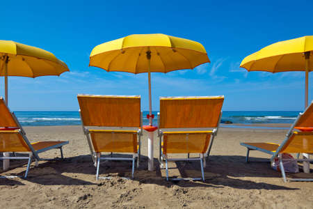 Empty lounge chairs under a yellow umbrella on a deserted beachの写真素材