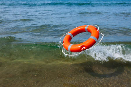 Red lifebuoy flying into the sea foamy waves on a sunny day at seaの写真素材