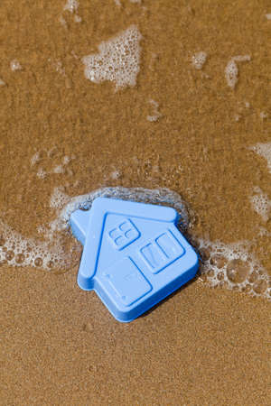 Blue toy plastic house on the sand washes waveの写真素材