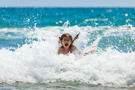 The little girl crying in the spray of waves at sea on a sunny dayの写真素材