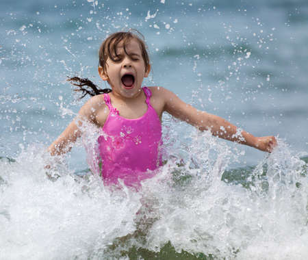 Little girl laughing and crying in the spray of waves at sea on a sunny dayの写真素材
