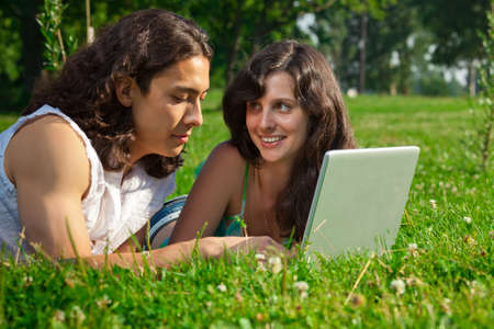The boy and girl lying on the grass in the park with a laptopの写真素材