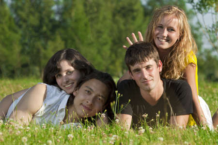 Four young men - two girls and two guys lying on the grass in the park and having funの写真素材