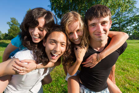 Four young people having fun in the park - boys ride girlfriends on the backの写真素材