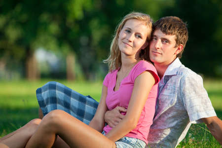 Two young lovers sitting on the lawn in the park and looks into the cameraの写真素材