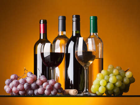 Several bottles of white and red wine, two glasses and grapes on an orange backgroundの写真素材