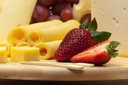 A set of different cheeses, strawberry and grapes on a wooden boardの写真素材