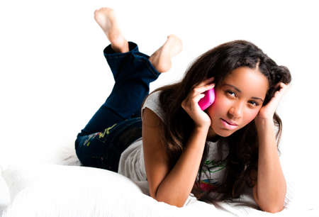 Concerned teenage girl on a pink cell phone lying down listening with legs crossed feet in the air - isolated on whiteの写真素材