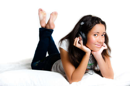 pretty teenage girl with headphones lying down listening to music with legs crossed feet in the air - isolated on whiteの写真素材