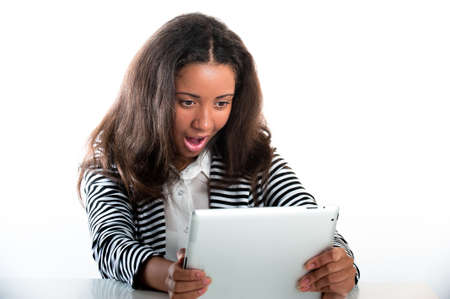 Beautiful mixed race teen girl, working with a portable tablet computer open mouthed in shockの写真素材