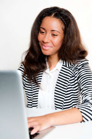 Beautiful mixed race teen girl, working and typing on a laptop computer at a desk looking satisfiedの写真素材