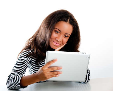 Beautiful mixed race teen girl, looking at a tablet computer hands in her elbows on a desk looking admiringly at the screenの写真素材