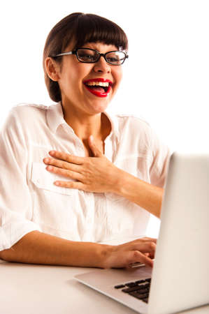 Professional young woman with glasses, sitting at a desk white with a laptop, laughing and surprisedの写真素材