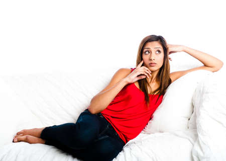 Beautiful asian indian teenage girl lying on the sofa, thinking, touching face and looking upの写真素材
