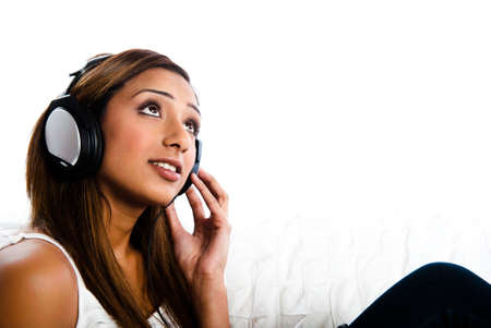 Beautiful asian indian teenage girl, listening to music with hand to headphone looking up and listening.の写真素材