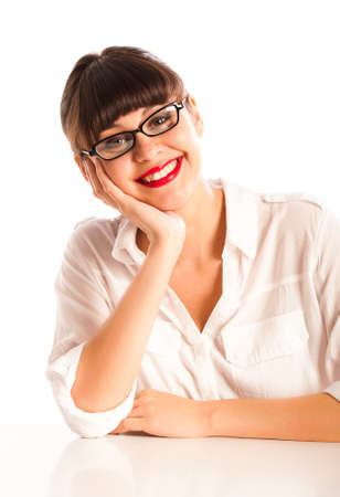 Professional young woman with glasses and red lipstick, sitting at a desk smiling with head resting on face. の写真素材