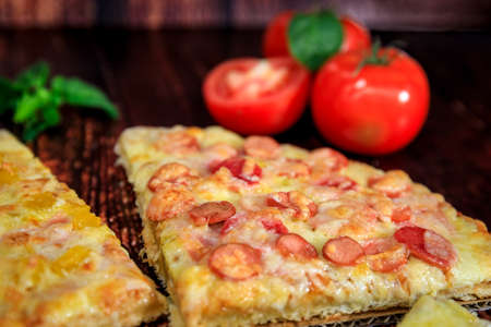 Closeup pizza slice with cabanossi, ham and cheese on brown wooden backgroundの写真素材