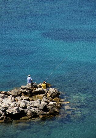 Two men angling with rod and line on seashoreの写真素材