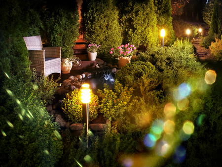 Illuminated home garden patio plants and evening party lights near small fountainの写真素材