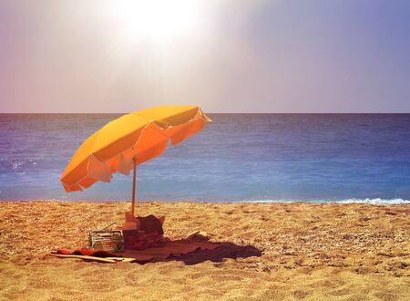 Yellow umbrella on hot sunny sandy beach by blue oceanの写真素材