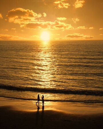 Male and female silhouettes meet at romantic sunset beachの写真素材