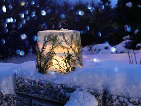 Frozen ice lantern with spruce twigs in snow, lit with candle lightの写真素材