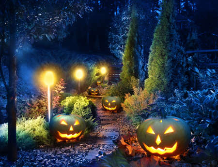 Dark home garden illuminated patio lights with halloween pumpkin lanterns along the pathの写真素材