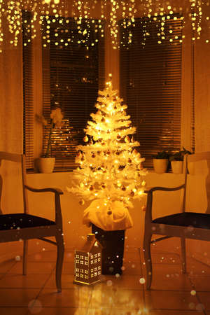 Illuminated white Christmas tree in front of a bay window, with decoration and string lightsの写真素材