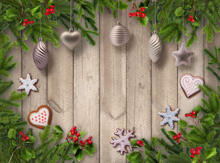 Green Christmas tree branches, red berries, gingerbread cookies and silver decoration balls on wooden vertical plank wall backgroundの写真素材