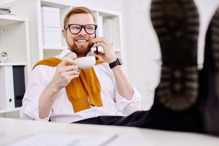 Mid age businessman drinking tea at the computer in the officeの写真素材