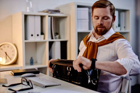 Mad age businessman looking at the clock in the evening officeの写真素材